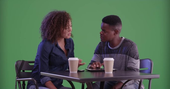 Young black man and woman have coffee on green screen. On green screen to be keyed or composited. 