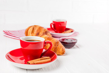 Freshly baked croissant on napkin, cup of coffee in red cup on white wooden background. French breakfast. Fresh pastries for breakfast. Delicious dessert. Closeup photography. Horizontal banner