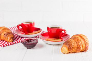 Freshly baked croissant on napkin, cup of coffee in red cup on white wooden background. French breakfast. Fresh pastries for breakfast. Delicious dessert. Closeup photography. Horizontal banner