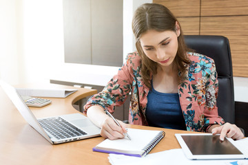 Woman checking note and tablet in her office.