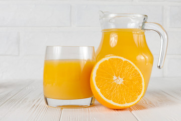 Fresh orange juice in glass and jug, half of citrus on white wooden background. Healthy eating, diet theme. Juicy fruit. Closeup photography. Horizontal banner