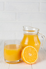 Fresh orange juice in glass and jug, half of citrus on white wooden background. Healthy eating, diet theme. Juicy fruit. Closeup photography. Vertical banner