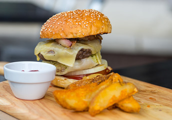 appetizing hot burger with beef chops melted cheese and vegetables sesame buns potato slices and sauce on a wooden board close-up