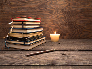 A stack of notebooks, a pen and a candle on a wooden table
