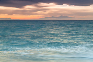 Crimson sunset on the shore of the orange sky and calm sea witt view at the mountains