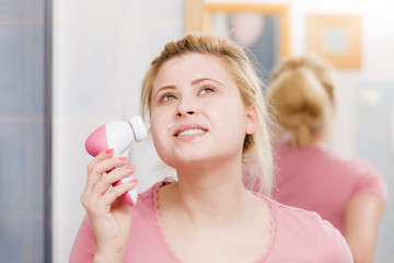 Happy woman using facial cleansing brush