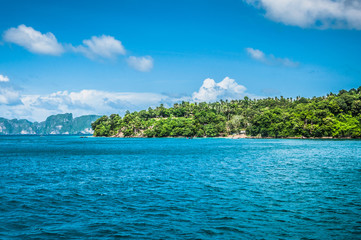 Green island in the middle of the ocean and blue cloudy sky on the background