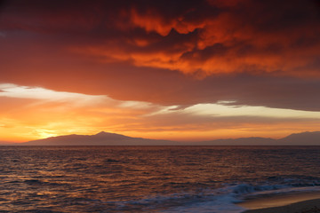 Crimson sunset on the shore of the orange sky and calm sea witt view at the mountains