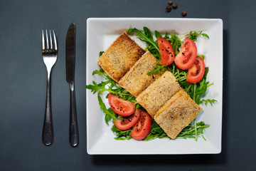 Salad of fried tofu with tomatoes and rocula. Homemade vegetarian salad in a white plate on a black background. A healthy Asian diet vegan vegetarian salad