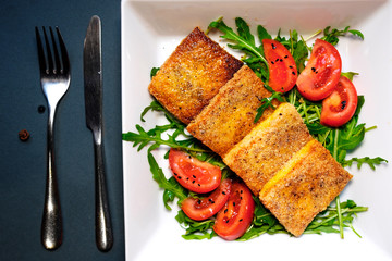 Salad of fried tofu with tomatoes and rocula. Homemade vegetarian salad in a white plate on a black background. A healthy Asian diet vegan vegetarian salad