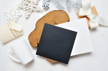 Fototapeta premium Mockup Christmas black greeting card letter in envelope and mug, flatlay on a white wooden background, with place for your text. Flat lay, top view photo mock up
