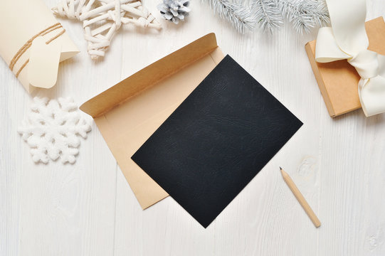 Mockup Christmas black greeting card letter in envelope and pencil, flatlay on a white wooden background, with place for your text, Flat lay, top view photo mock up