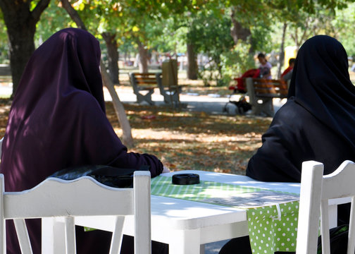 two Muslim women in a paranjas sitting at a table in a cafe in the park