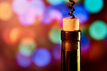 A bottle of wine with a cork and a corkscrew on the background of a colorful bokeh. Copy space.