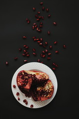 Ripe freshness red pomegranate with seed, grains on white plate on dark background. Dissected pomegranate on pieces.