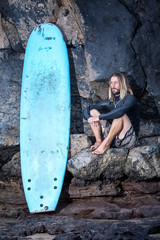 Surfer sitting next to surfboard looking at the sea