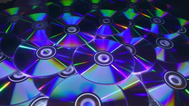 Many compact discs lying on top of each other rotate and shimmer in different colors. On they fall several CDs. Closeup. Slow mo, slo mo, slow motion, high speed camera, 240fps, 250fps
