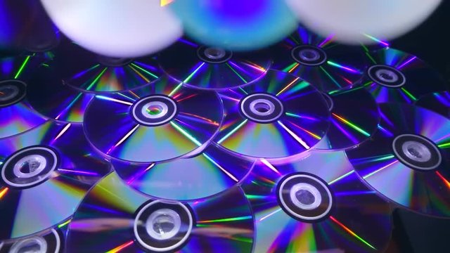 Many compact discs lying on top of each other rotate and shimmer in different colors. On they fall several CDs. Closeup. Slow mo, slo mo, slow motion, high speed camera, 240fps, 250fps
