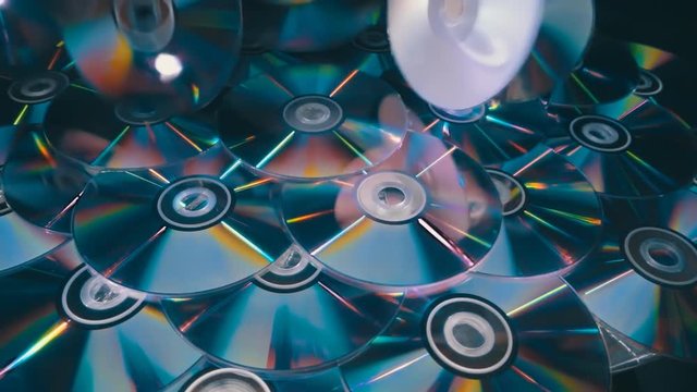 Many compact discs lying on top of each other rotate and shimmer in different colors. On they fall several CDs. Closeup. Slow mo, slo mo, slow motion, high speed camera, 240fps, 250fps
