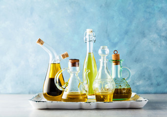 different shapes, types and sizes of cruets with olive oil on the table on a tray on blue