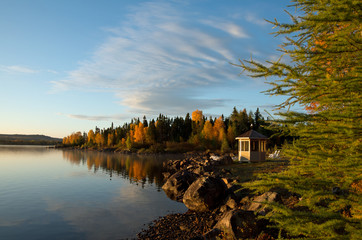 Sunrise highlights the autumn colors and a gazebo near a calm lake. 