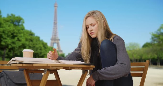 Young white Parisian student studies for midterm near Eiffel Tower
