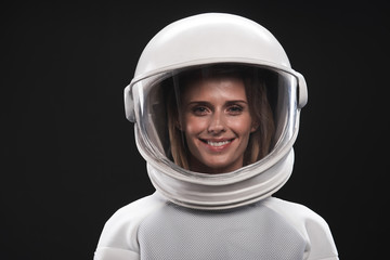Feeling happiness. Portrait of charming delighted female astronaut wearing helmet and protective suit is standing and looking at camera with wide smile. Isolated background © Yakobchuk Olena