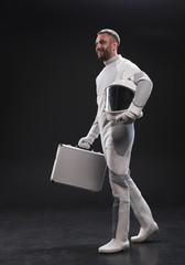 Important appointment. Full-length of cheerful bearded astronaut in protective suit is standing with helmet and carrying his suitcase while looking aside with smile. Business in space concept