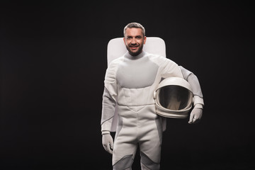 Portrait of happy astronaut is holding helmet while standing in white protective suit. He is looking at camera with joy. Isolated background with copy space in left side. Spaceman concept