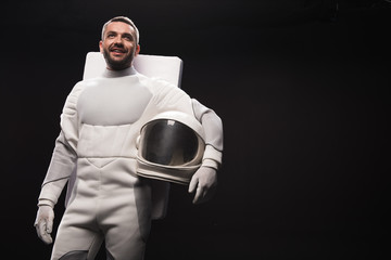 Portrait of cheerful spaceman is standing in hyperbaric astronaut protective suit and looking ahead with bright smile. He is holding white helmet. Isolated background with copy space in right side
