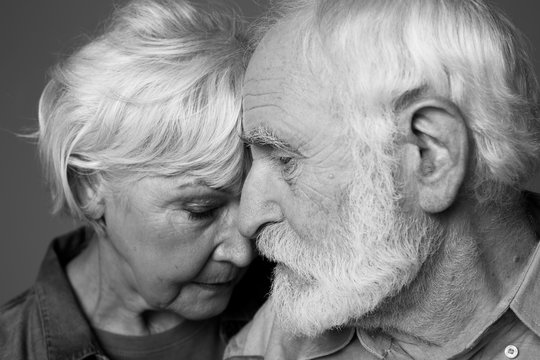 Close up black-and-white portrait of grey-haired man and woman standing closely. Isolated on grey background