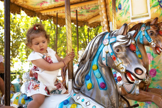 Happy female toddler ridding colorful carousel horse.