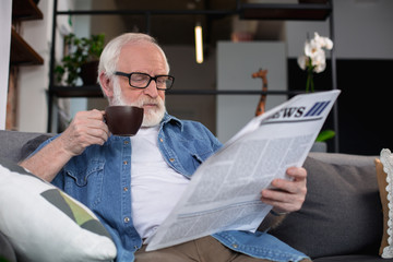 Interesting hobby. Waist up portrait of thoughtful pensioner enjoying daily journal while holding mug of hot drink