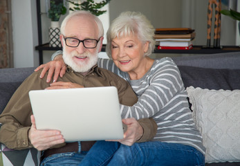 Free time together. Half-length portrait of mature couple relaxing on couch at home while looking in computer