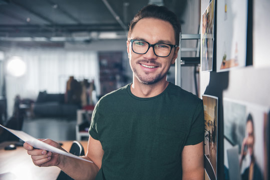 Portrait of smiling bearded man keeping photos in arm while locating in apartment. Occupation concept