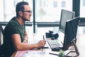 Side view orderly bearded retoucher working with graphic electronic tablet while situating at desk. Occupation concept