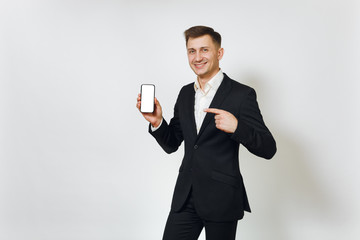 Young successful handsome rich business man in black suit pointing at modern mobile phone isolated on white background for advertising. Concept of money, achievement, career and wealth in 25-30 years.