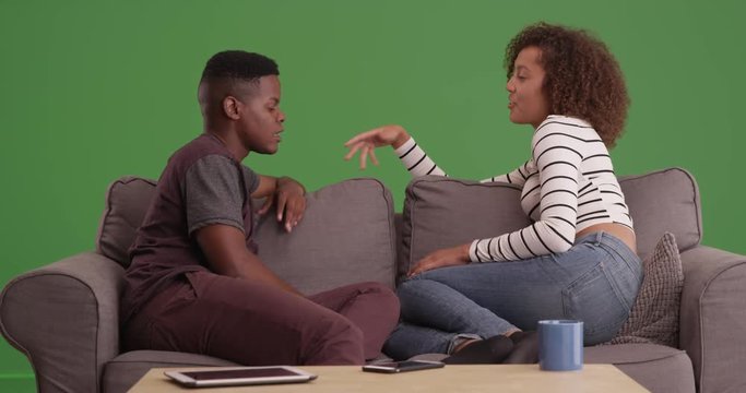 African American man and woman talk while relaxing on their couch on green screen. On green screen to be keyed or composited. 