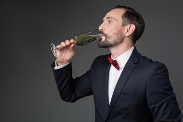 Side view profile of confident man tasting sparkling wine from glass. He is standing in formal suit. Isolated and copy space
