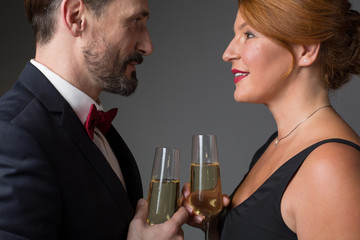 Side view of happy senior man and woman looking at each other with fondness. They are holding glasses and smiling. Anniversary celebration concept. Isolated