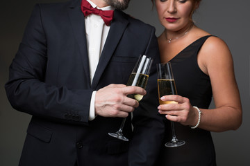 Close up of arms of mature loving couple clinking glasses of champagne. They are standing in fancy suit and dress