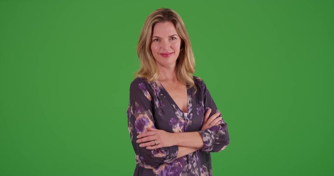 Caucasian woman with arms crossed, smiling at camera on green screen. On green screen to be keyed or composited.