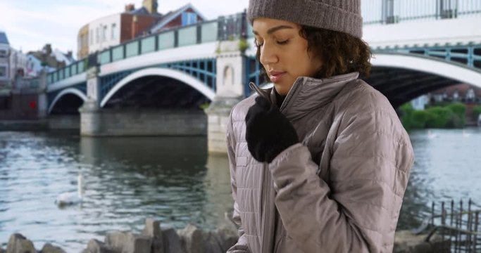 Attractive black female zips up her jacket on cold day in Windsor by Eton Bridge