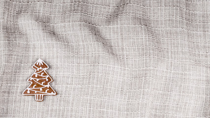 Hand-decorated Christmas gingerbread on beige crumpled fabric. Background from cloth texture and pastry in christmas tree shape with copy space.