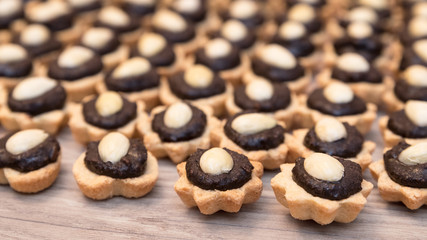 Detail of coconut cupcakes with chocolate filling and almond garnish. Decorative sweet Christmas pastry stacked on a wood background. Small depth of sharpness.