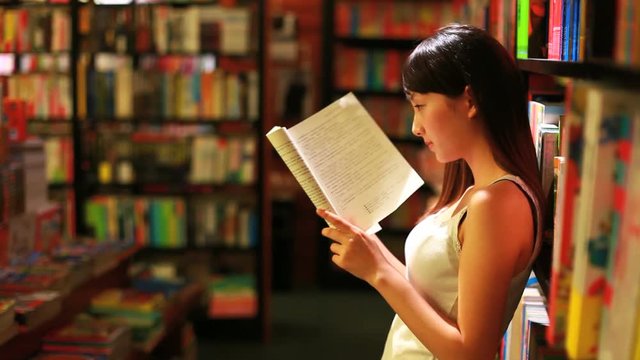 young woman reading book in bookstore