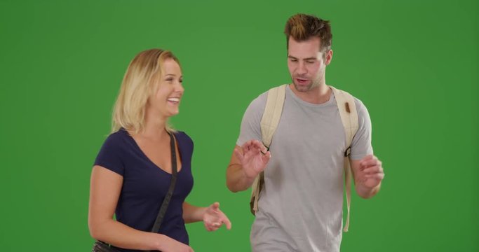 Young white couple walking with backpacks and talking on green screen. On green screen to be keyed or composited. 