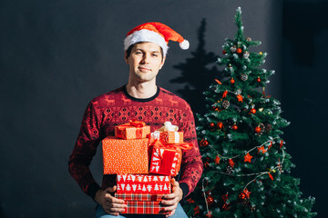 Handsome smiling male with red gift box in hands over christmas tree.