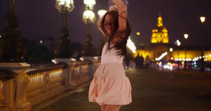 Young attractive Hispanic female dances around happily on the Pont Alexandre. Excited Latina youth hops around joyously on a beautiful Parisian night. 4k