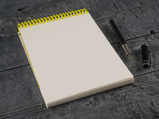 Notebook with yellow cover and black fountain pen on a wooden table.